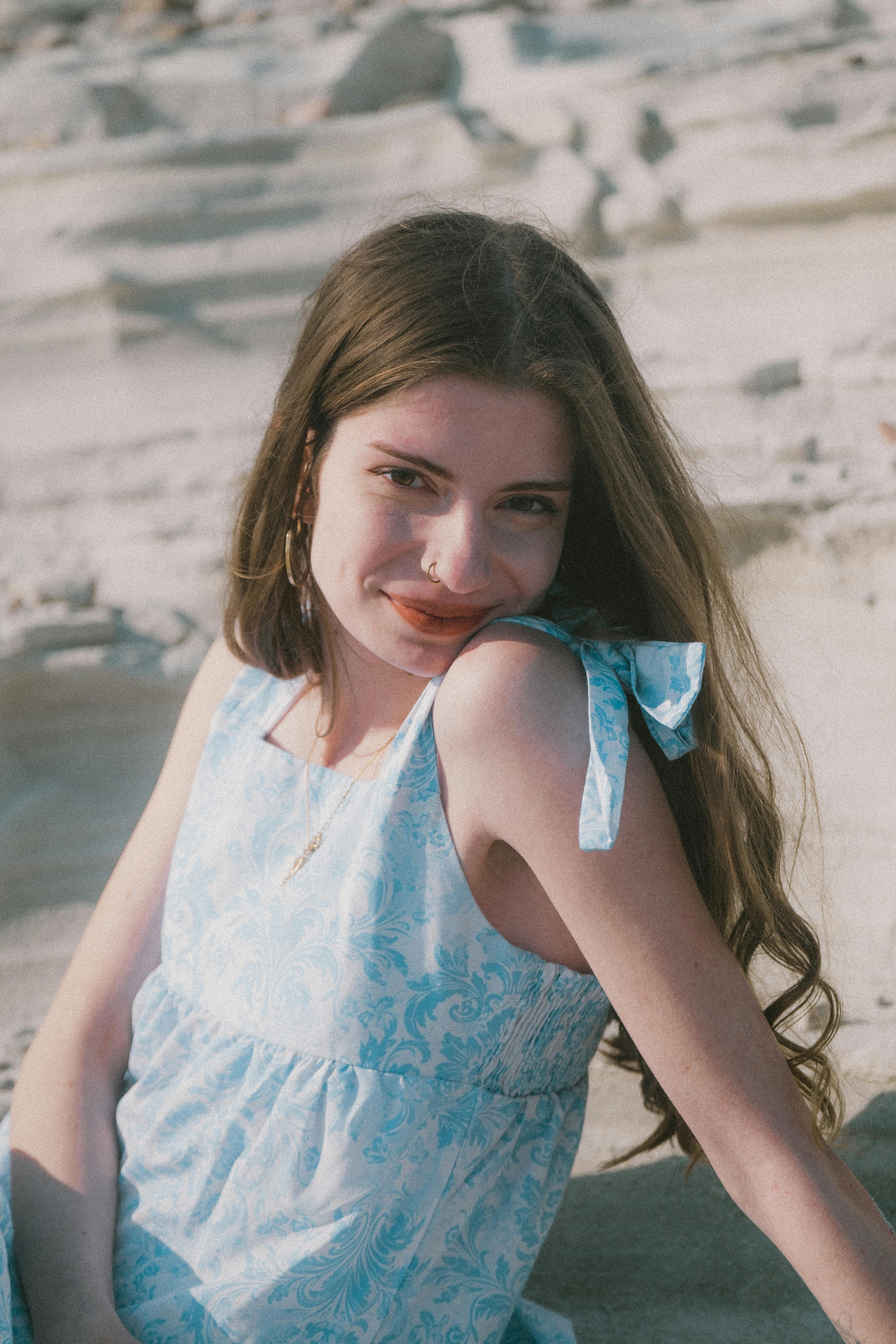A woman in a blue dress enjoys a sunny day at the beach, exuding natural beauty and relaxed style.
