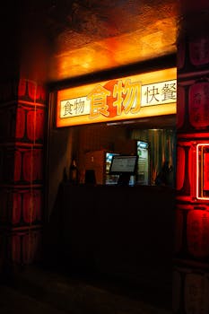 A vibrant Asian food stall glowing under neon lights with cultural decor and text.