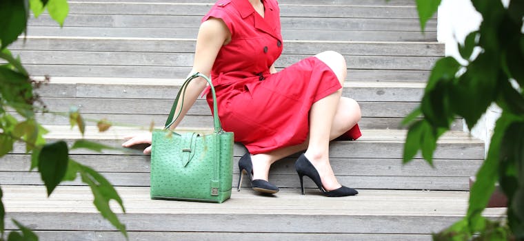 A stylish woman in a red dress sitting on stairs with a green handbag. Modern fashion statement.