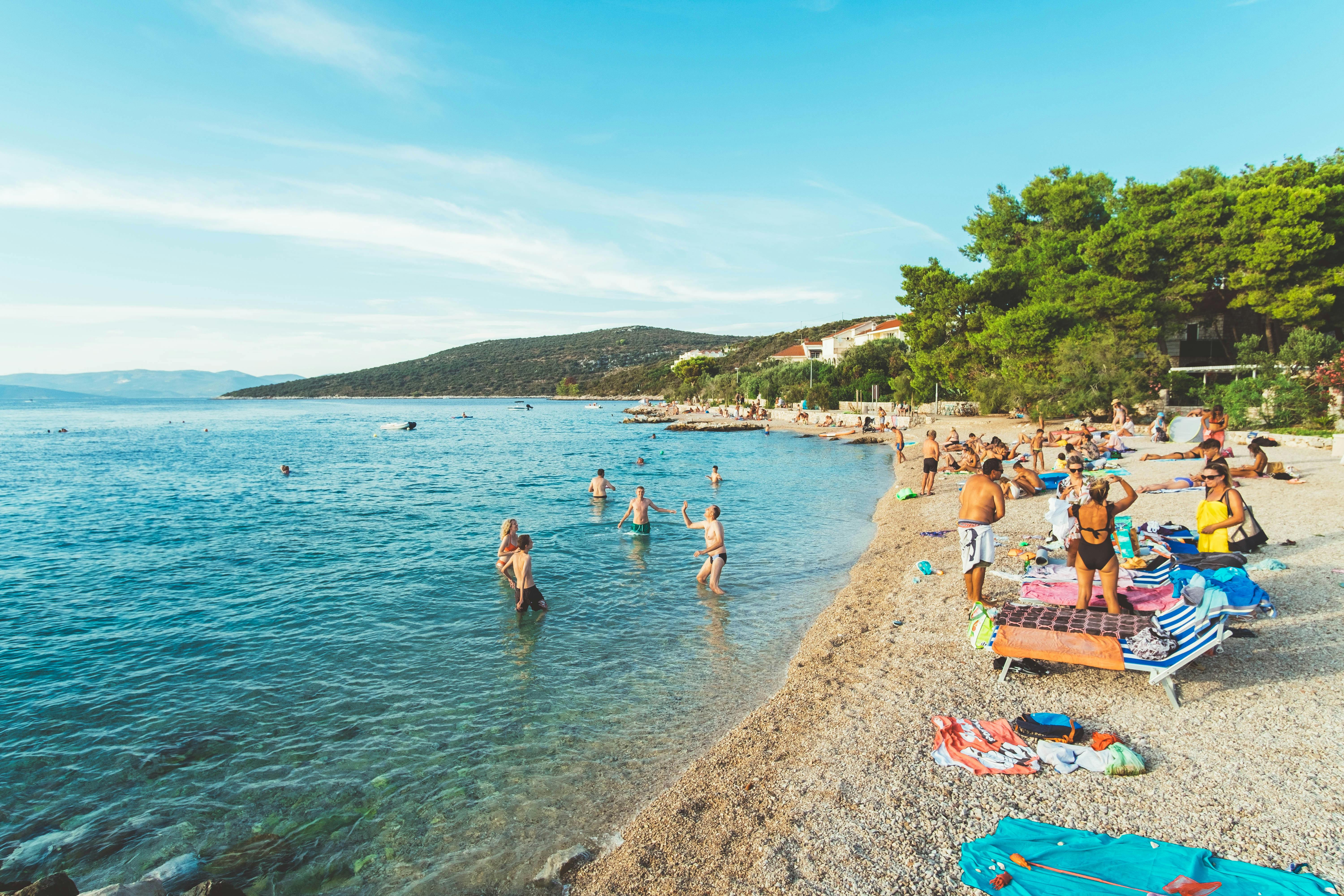 Picturesque beach scene in Skradin, Croatia with sunbathers and swimmers enjoying a sunny summer day.