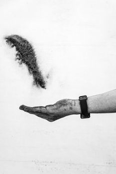 Minimalist monochrome image of sand flowing from a hand, symbolizing time and nature.