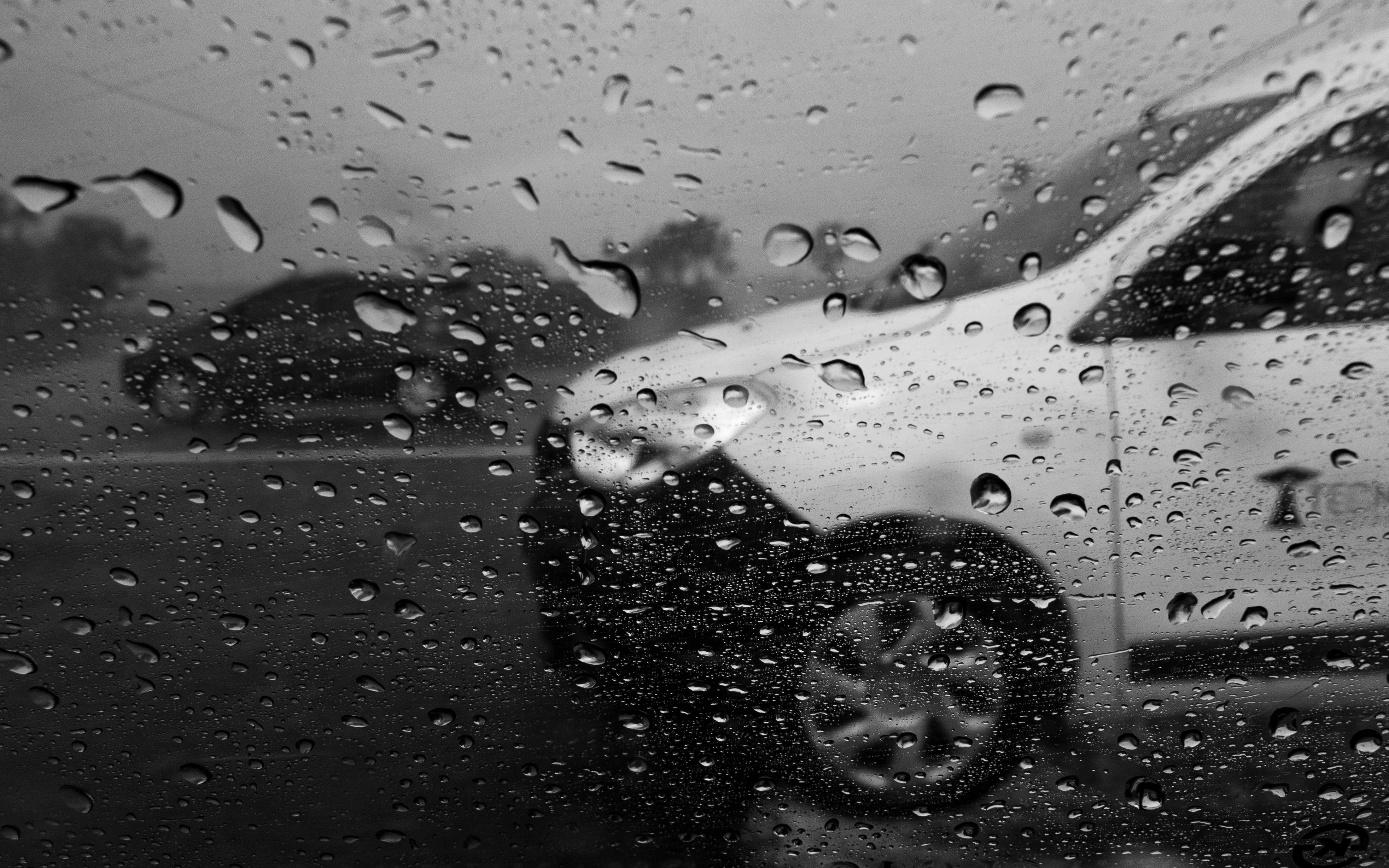 Black and white view through a rainy window at Mar del Plata, Argentina, capturing cars in motion.