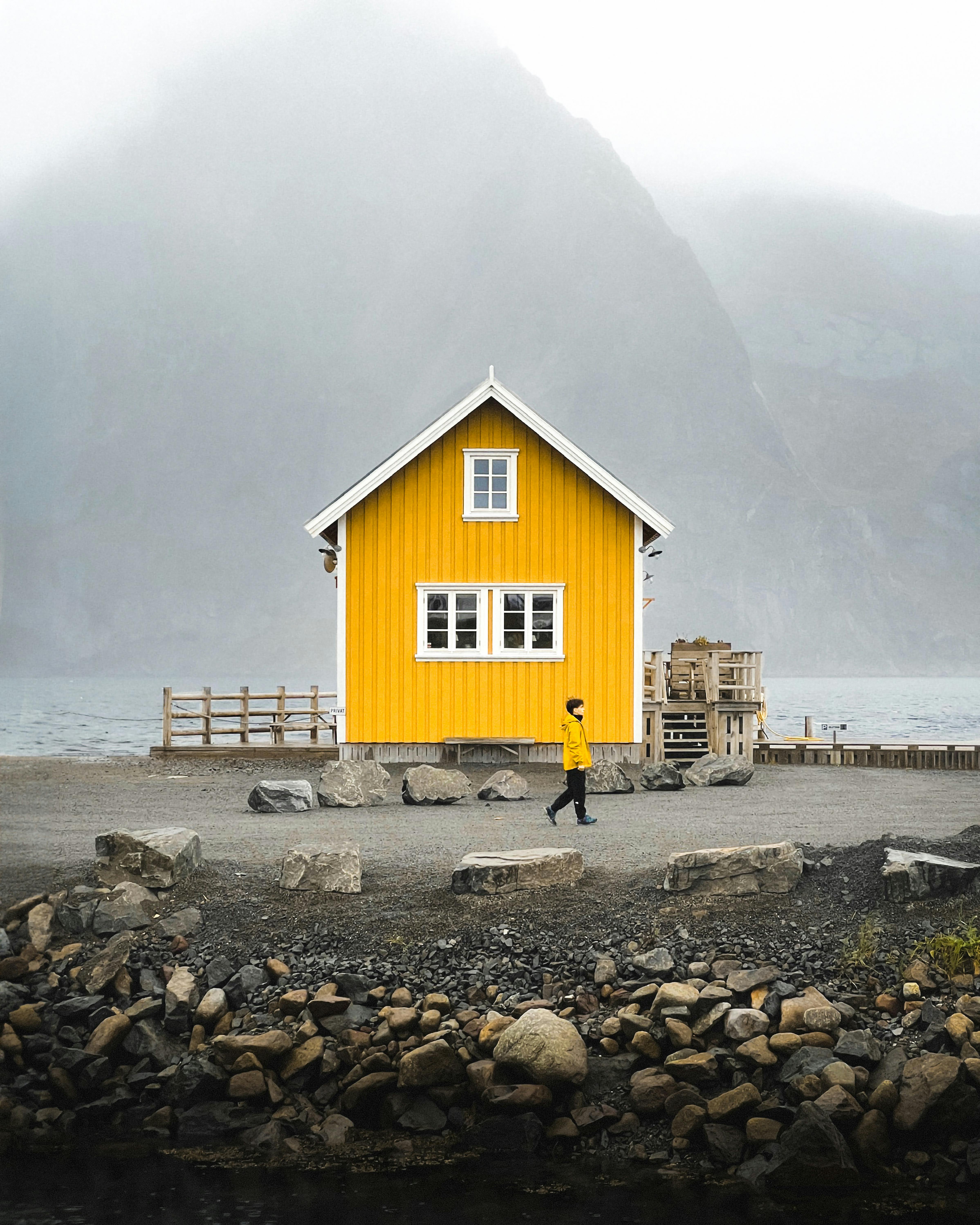 Yellow house in Nordland, Norway, surrounded by misty mountains and serene seascape.
