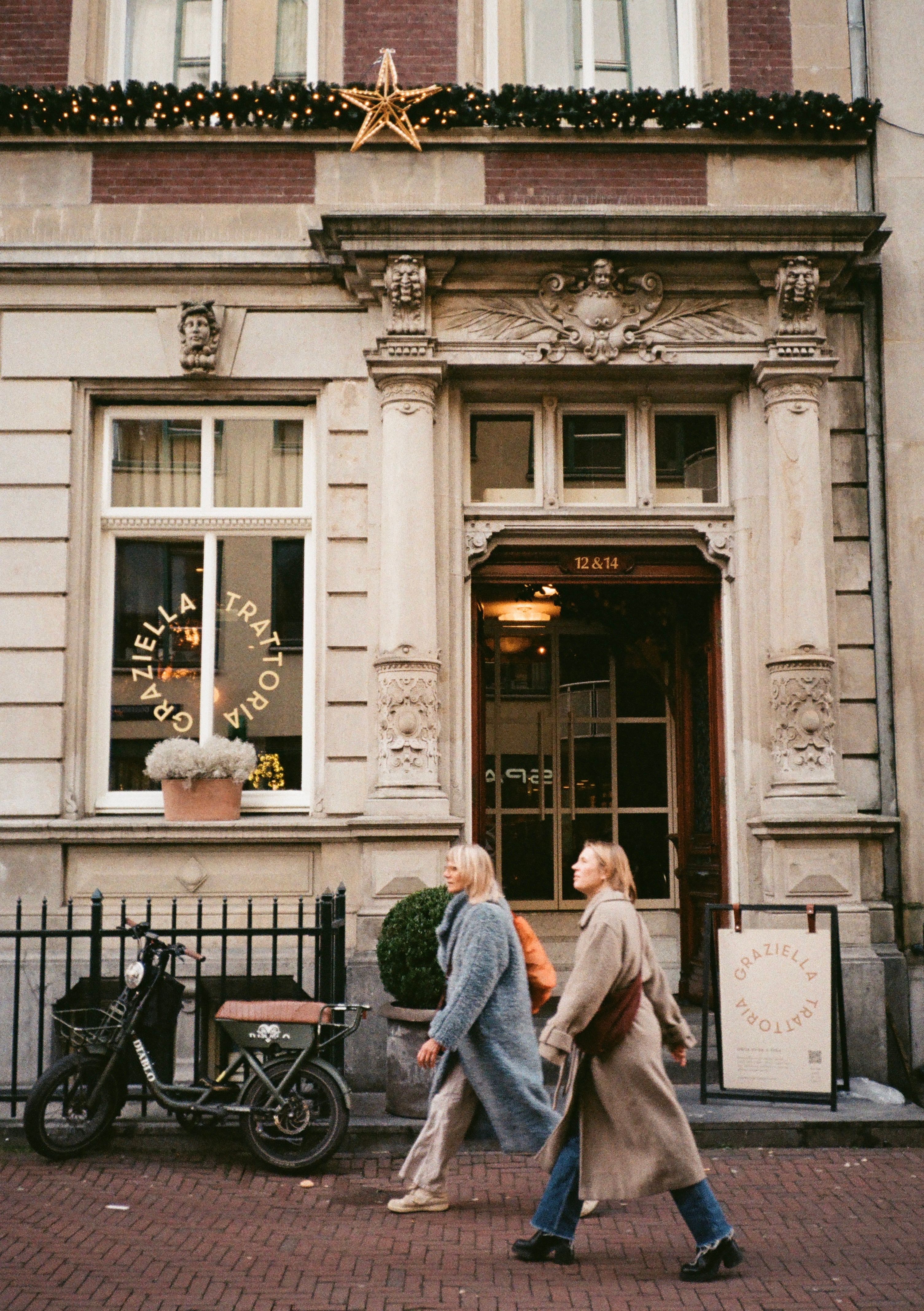 Two women walking by a vintage building in Amsterdam, Netherlands, during the day.