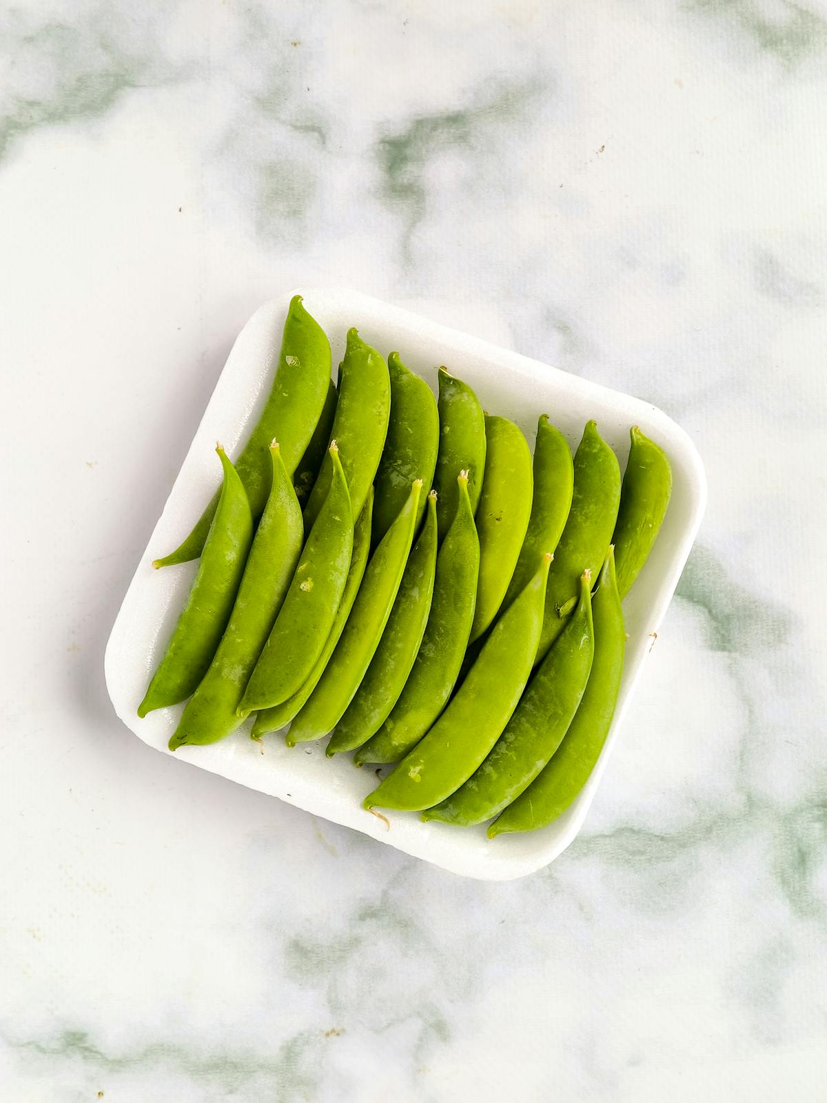 Piselli verdi freschi disposti ordinatamente su un vassoio bianco visto dall'alto