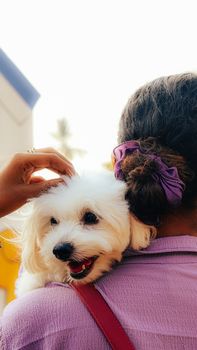 A woman carrying a fluffy white dog on her shoulder outdoors, showcasing companionship.