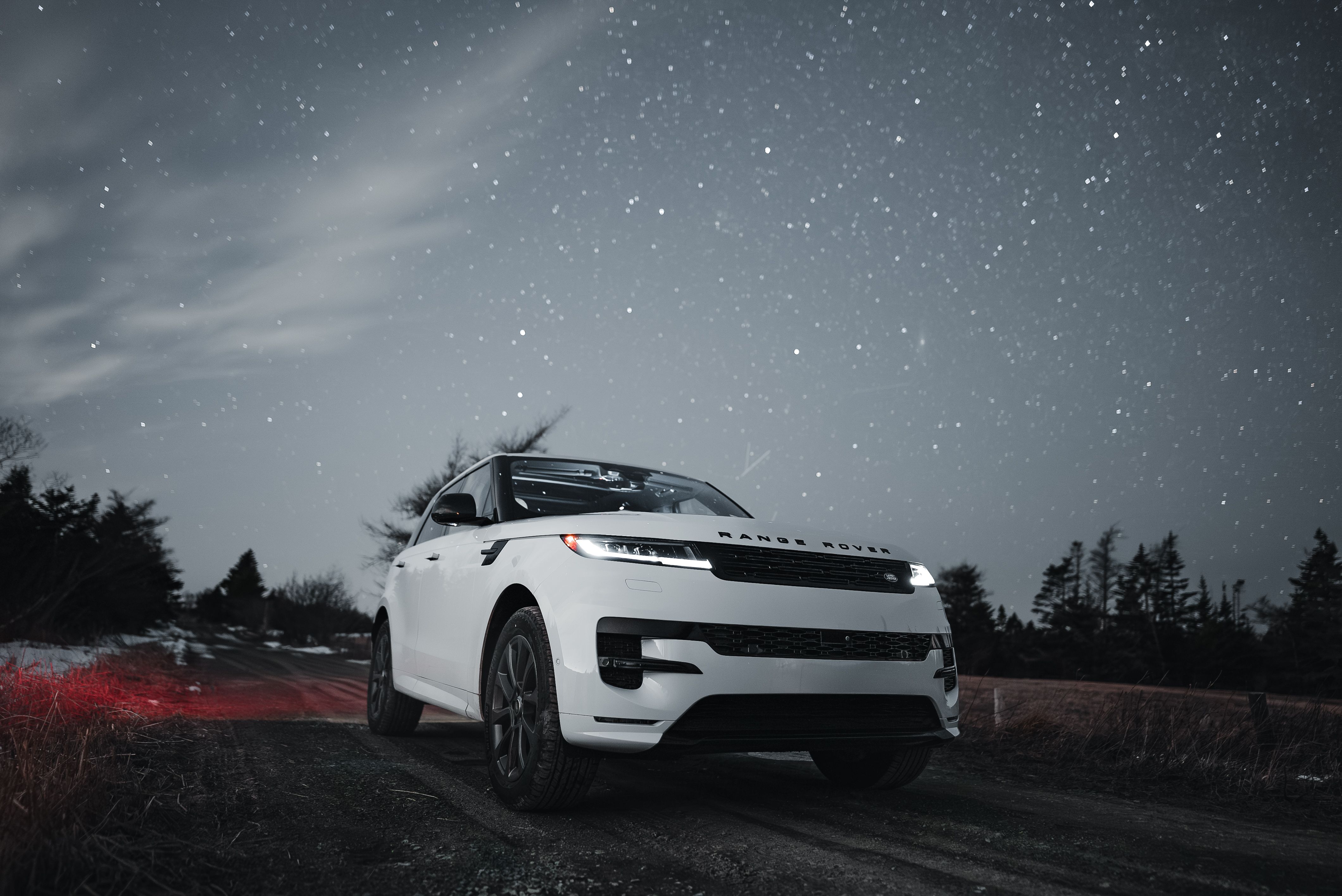 White luxury SUV parked on a winding road under a starry night sky, with mountains in the background.