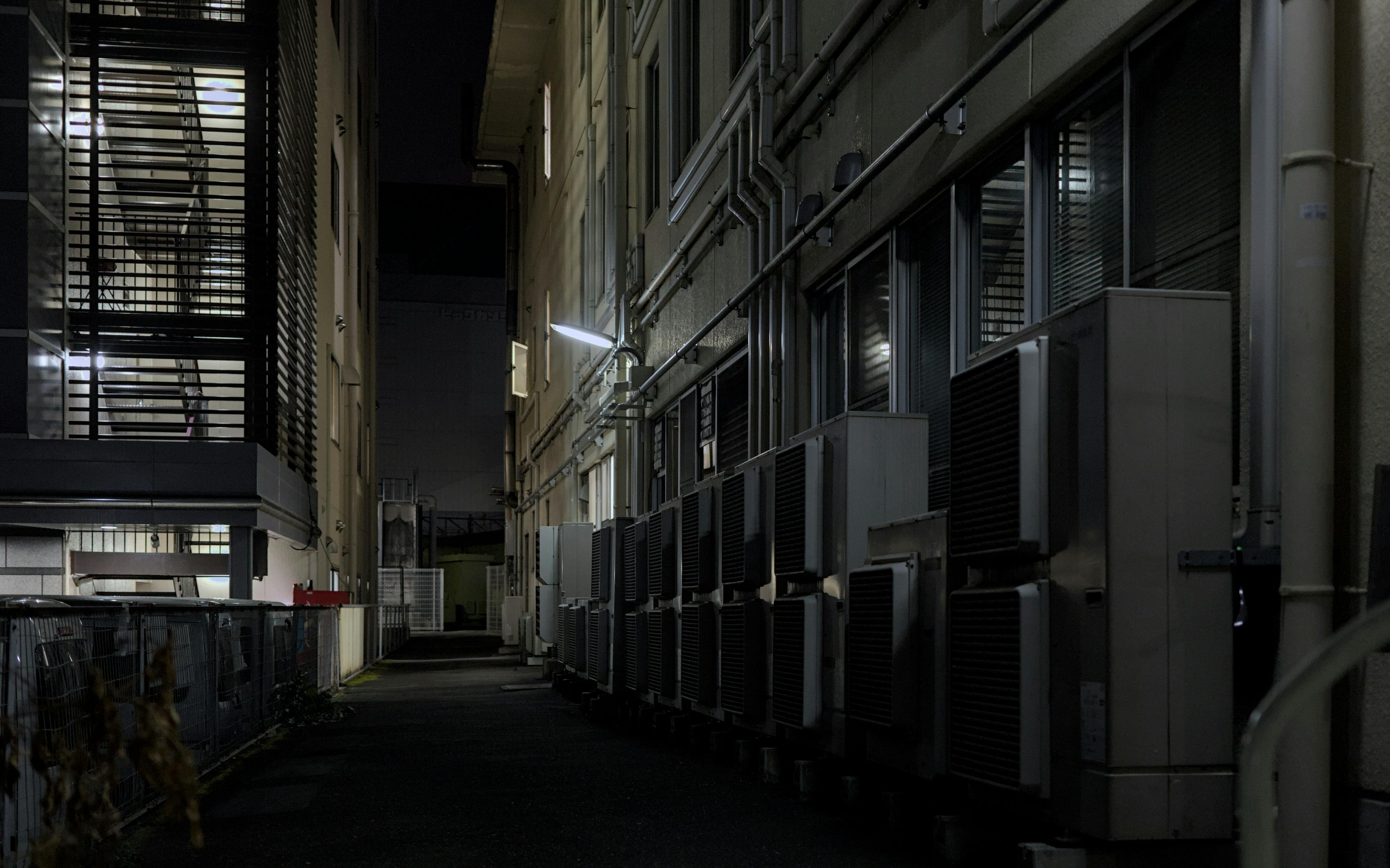 A dimly lit urban alley in Kyoto featuring air conditioning units, captured at night.
