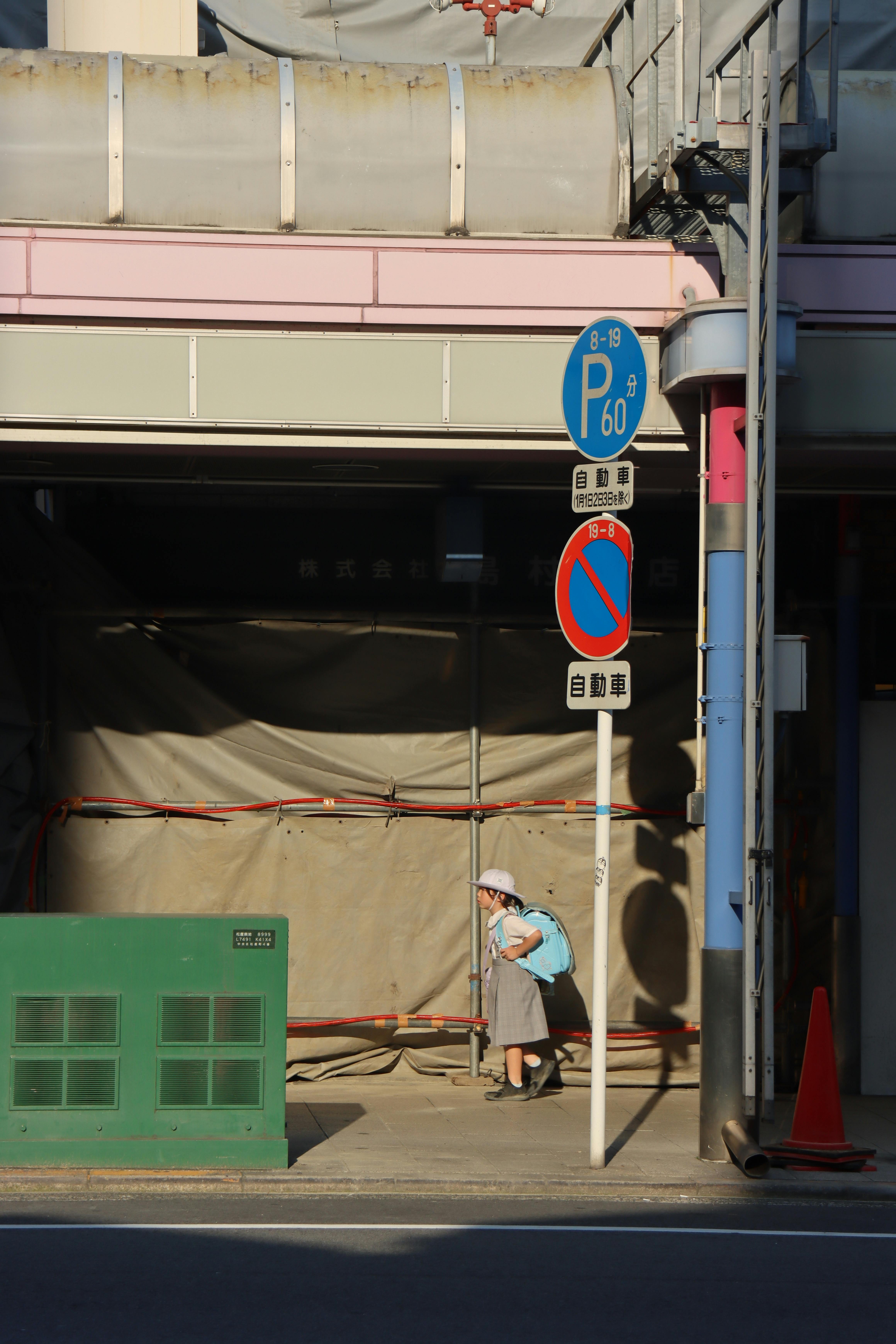 Elderly woman walks beneath construction site surrounded by urban signage.
