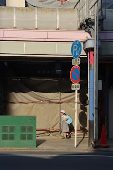 Elderly woman walks beneath construction site surrounded by urban signage.