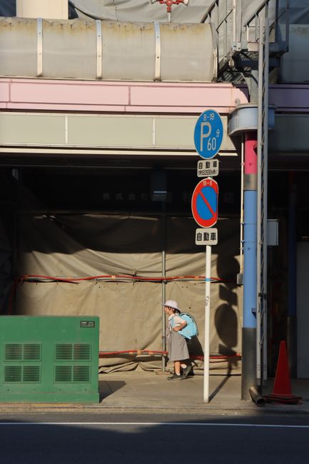 Elderly woman walks beneath construction site surrounded by urban signage.