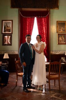 A couple poses elegantly in a vintage-style room with rich decor and ambient lighting.