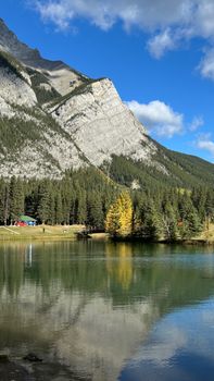 Beautiful mountain landscape with lake reflection, evergreen trees, and clear blue sky in daylight.