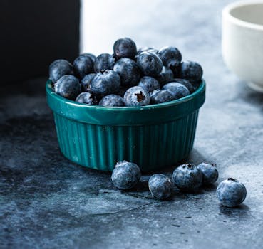 A ceramic bowl filled with fresh blueberries on a dark surface, showcasing healthy food.