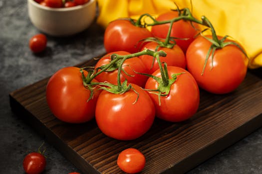 Vibrant fresh red tomatoes on a wooden board with a dark aesthetic.