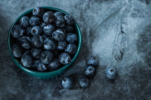 Free A bowl of fresh blueberries on a textured background, emphasizing a dark aesthetic. Stock Photo