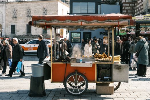 A vibrant street cart selling food amidst a busy Istanbul market square.