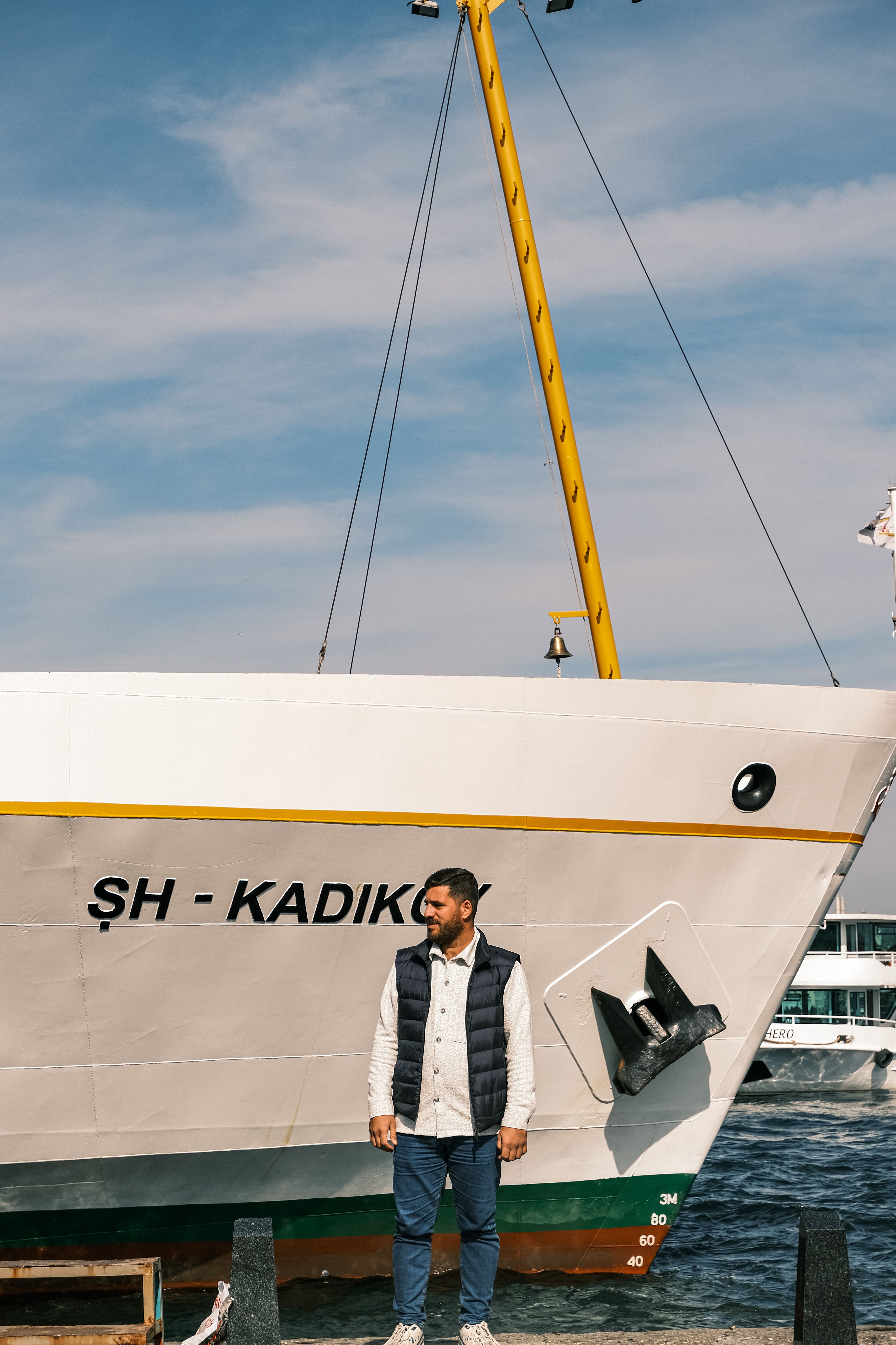 A man stands by a large ship under a clear blue sky, showcasing maritime travel.