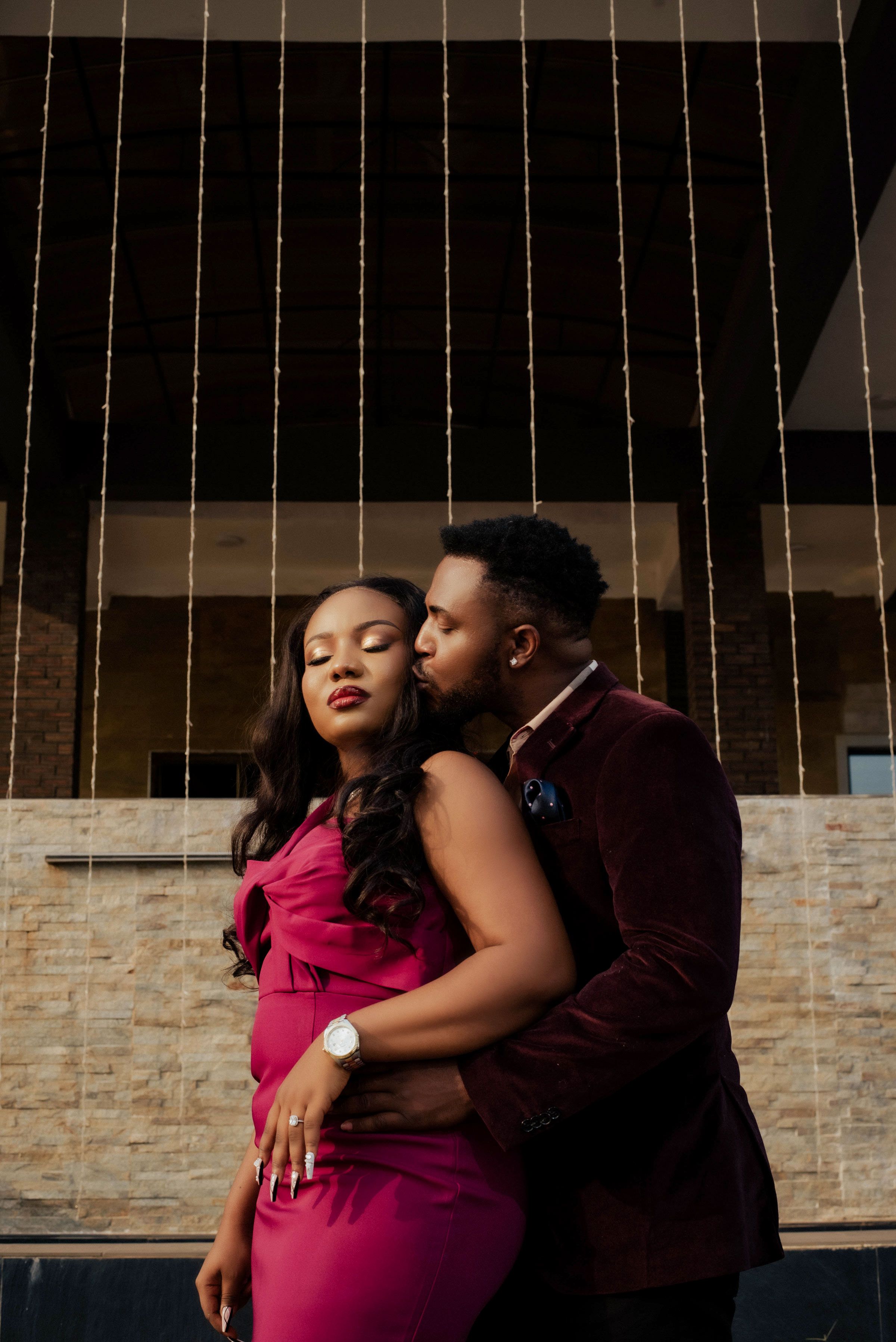 Sophisticated couple in evening wear embracing against a textured wall backdrop.