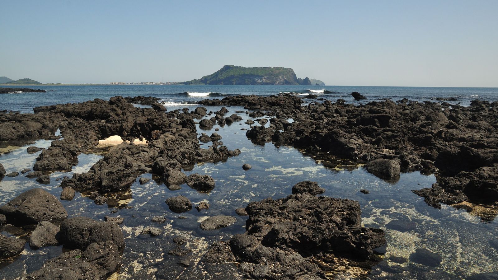 Batuan vulkanik hitam di tepi laut yang menjadi ciri khas wisata pulau jeju korea selatan
