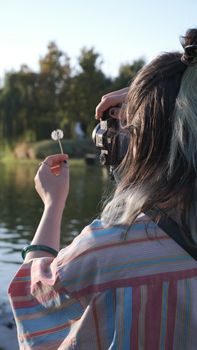 Young woman captures nature scenes using a vintage camera near a serene lakeside during a sunny day.