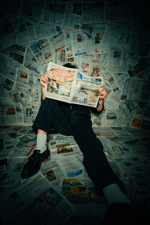Free Person sitting on floor covered with newspapers, reading in a creative setup. Stock Photo