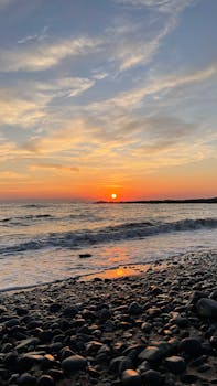 Beautiful sunset over pebbled beach at Armutlu, Türkiye. Vibrant colors reflect on the sea and sky.