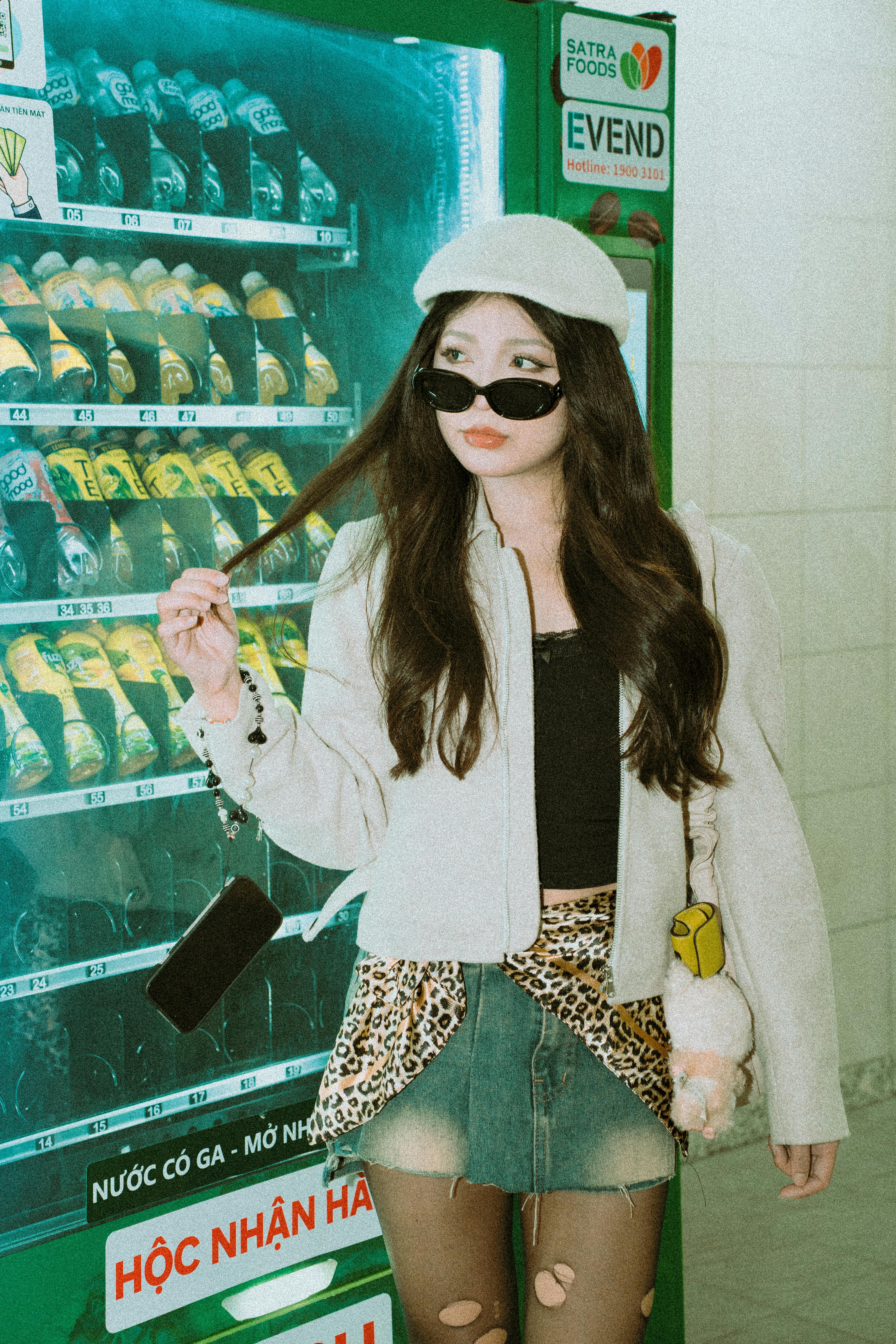 Stylish woman poses with a vending machine, showcasing modern fashion trends.