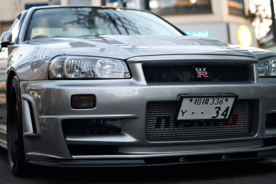 東京の路上に駐車された、象徴的なデザインを披露する銀色の日産スカイライン R34 GTR のクローズアップ。