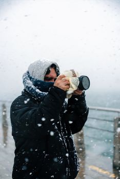 A person photographing a winter scene amidst falling snow on a boardwalk.