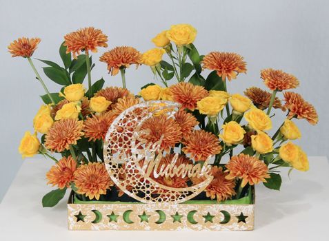 A vibrant display of orange chrysanthemums and yellow roses with Eid Mubarak decor.