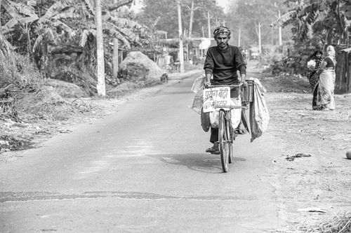 Free A rural scene in India showing a man cycling with goods on a village road. Stock Photo