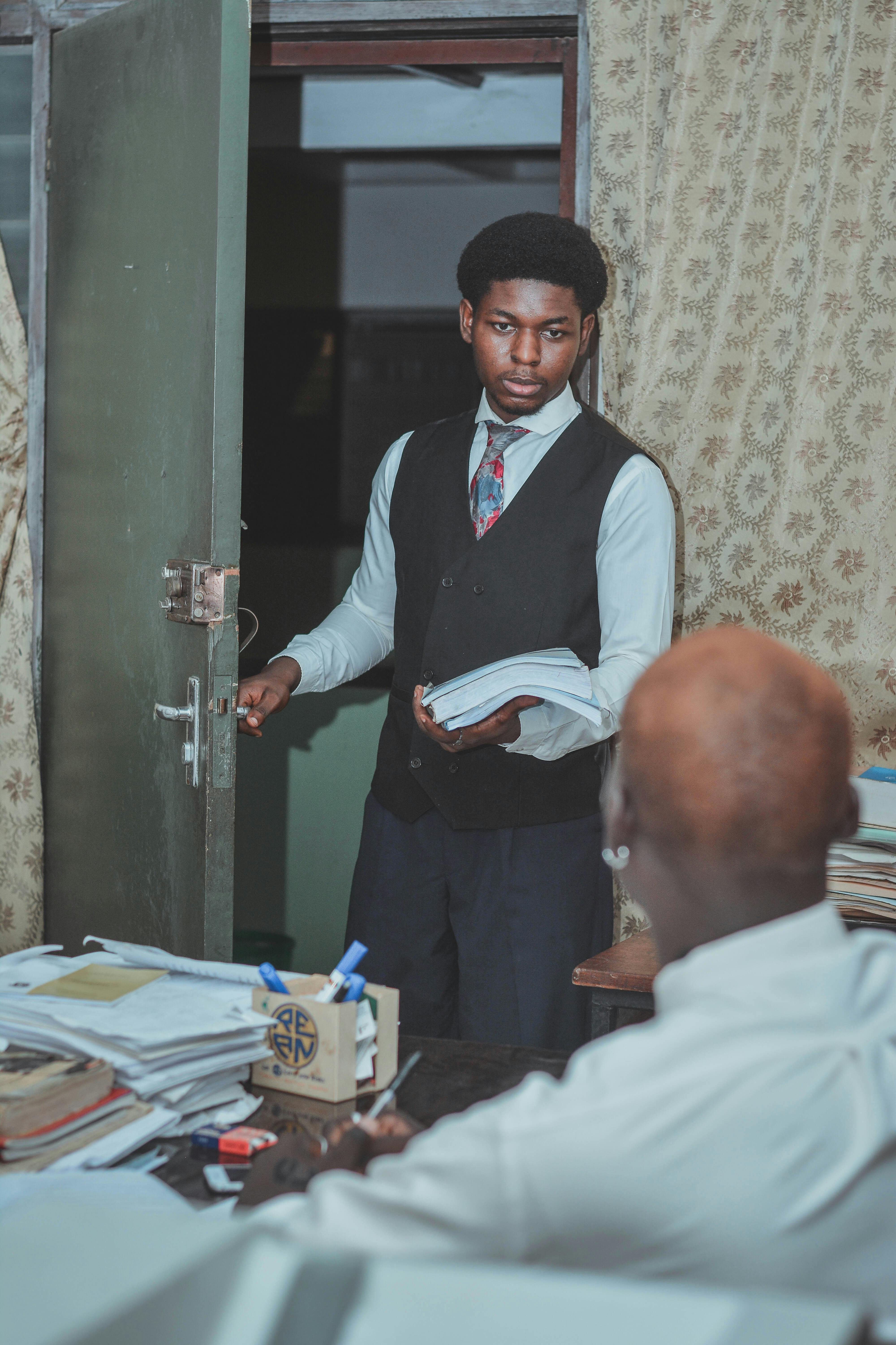 Gratis Un giovane uomo in abito formale entra in un ufficio con in mano dei documenti, che descrivono un ambiente professionale. Foto a disposizione