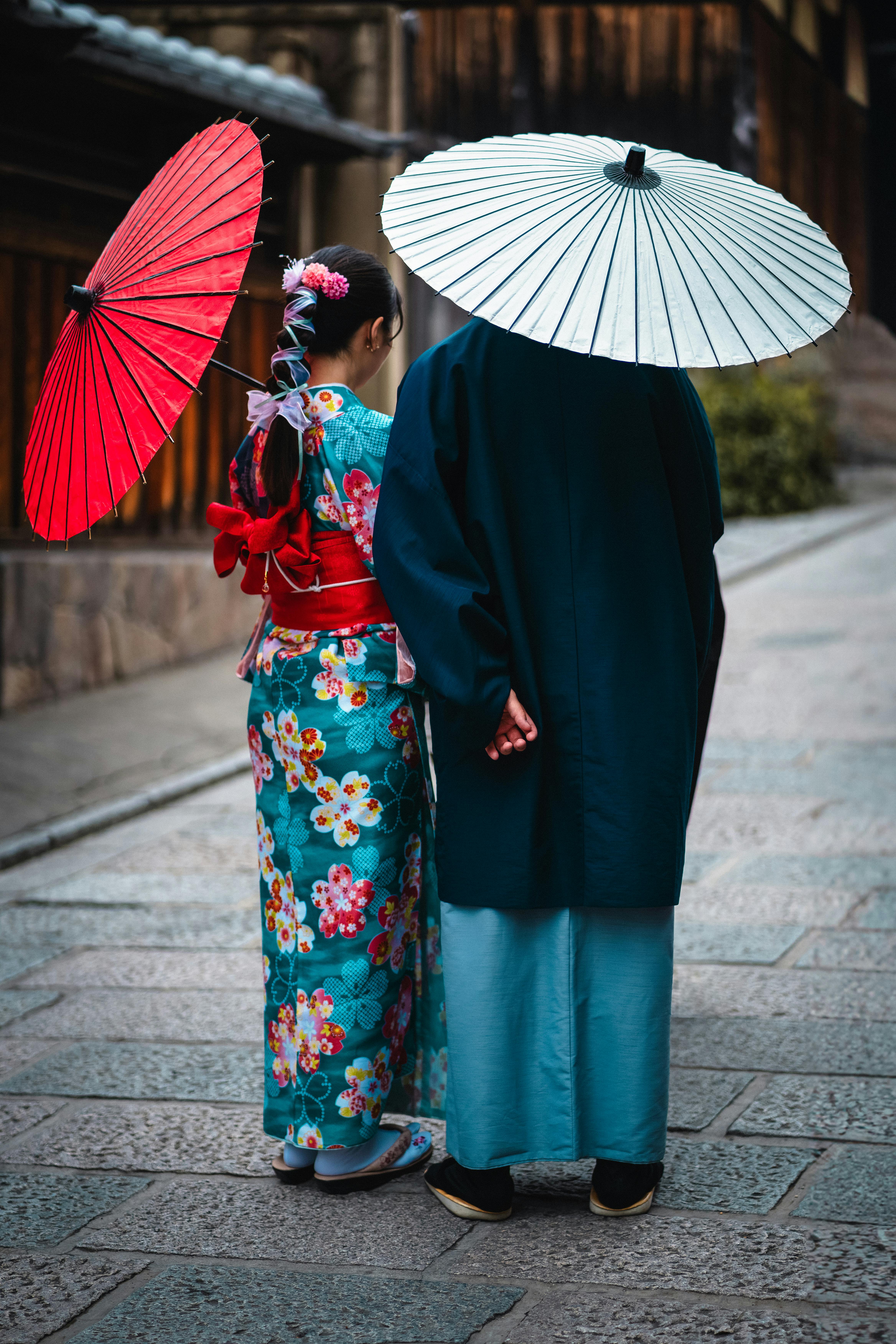A couple wearing traditional kimonos and umbrellas walking in Kyoto, Japan.