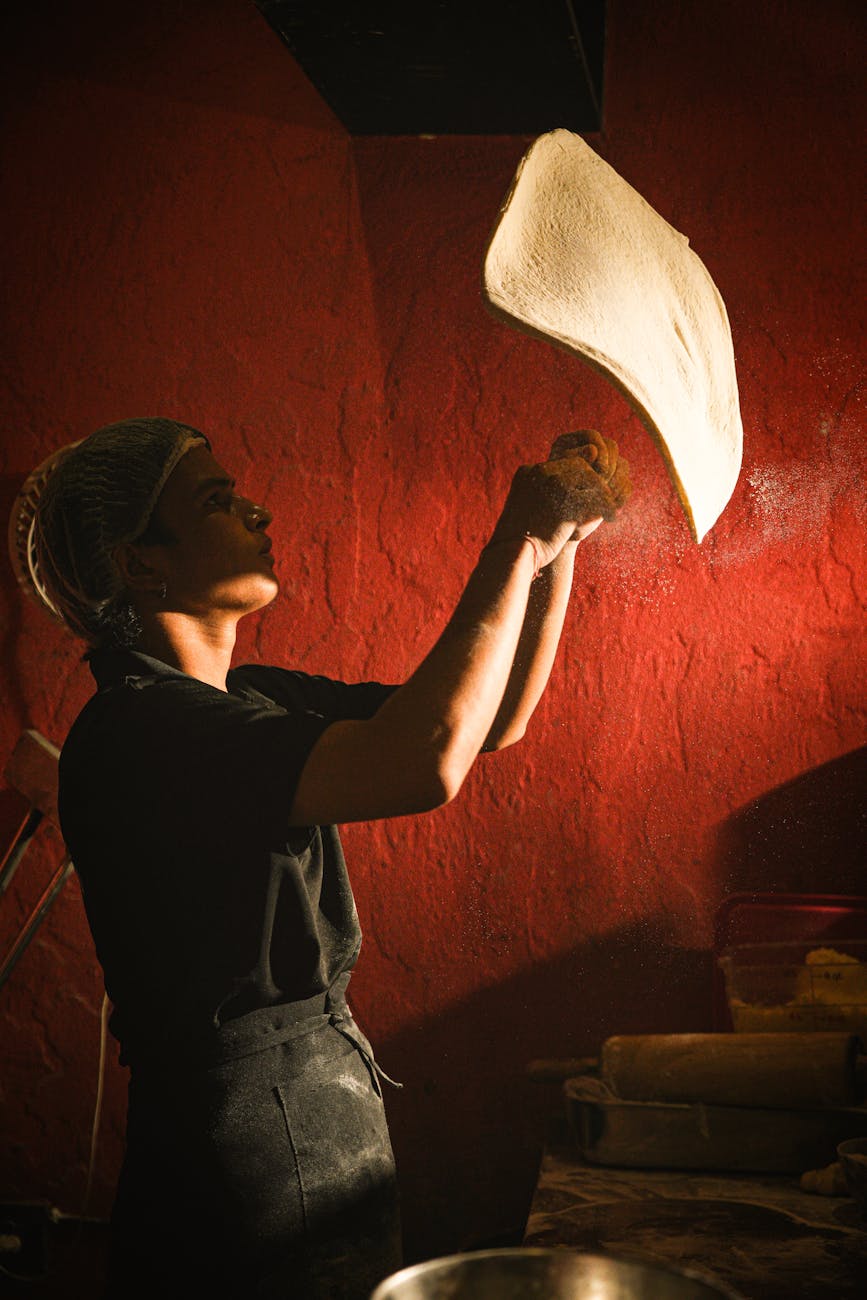A chef skillfully tosses pizza dough in a warmly lit kitchen.