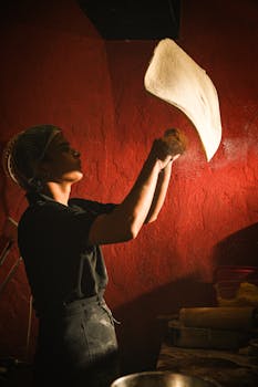 A chef skillfully tosses pizza dough in a warmly lit kitchen, showcasing traditional culinary artistry.