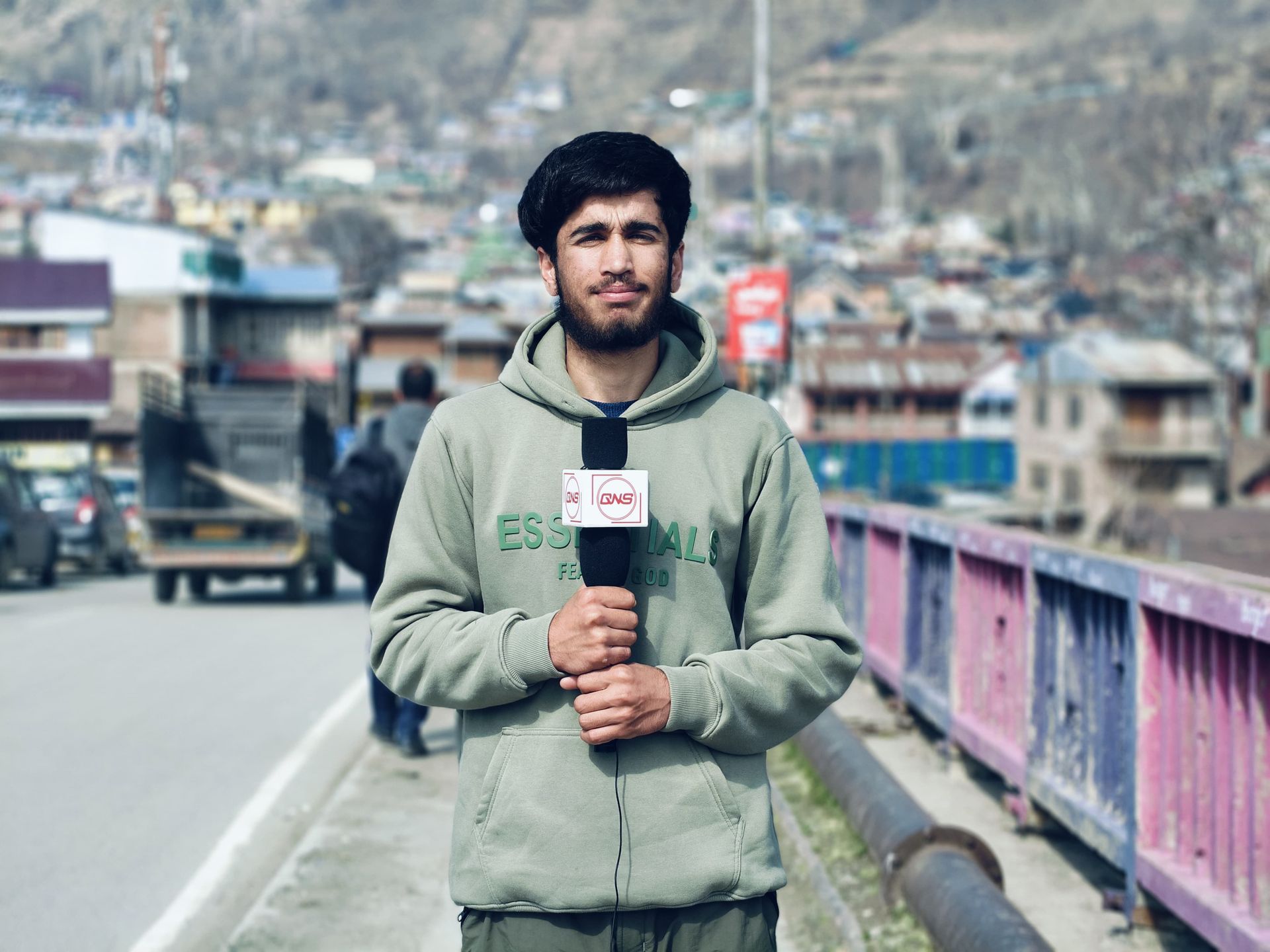 Young male reporter holding a microphone on a city street, reporting news.
