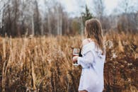 秋天，一名妇女穿着白衬衫，端着酒杯站在乡村田野里