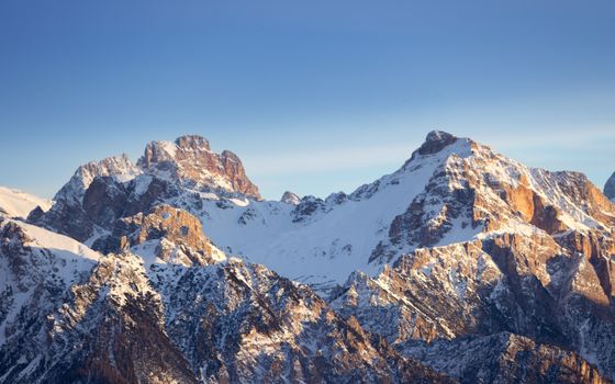 Stunning view of the Dolomites with snowy peaks illuminated by the golden hour sunlight.