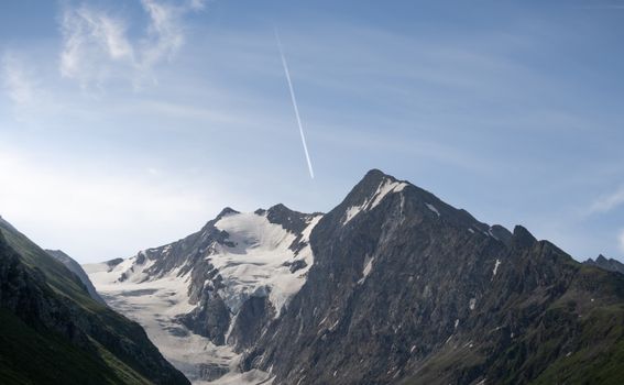 Snow-covered mountain peaks under a clear blue sky with a plane streak in Obergurgl, Austria.
