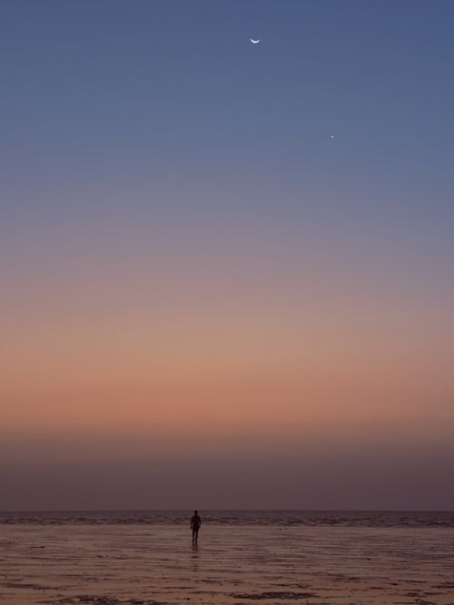 Free A peaceful Indian beach at sunset with a crescent moon and lone figure in silhouette. Stock Photo