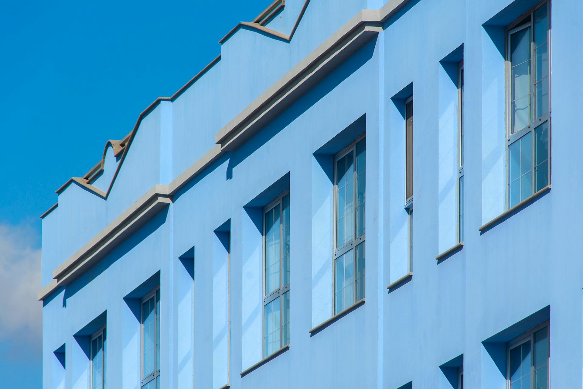 Daytime shot of a modern blue building facade with windows and architectural details under a clear sky.