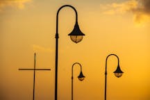 Silhouette of lampposts and a cross against a warm sunset sky.