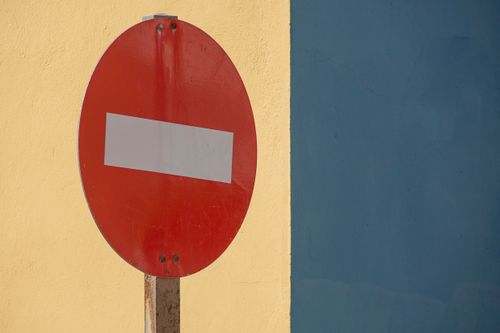 Free A red no entry sign against a vibrant yellow and blue wall, ideal for urban themes. Stock Photo