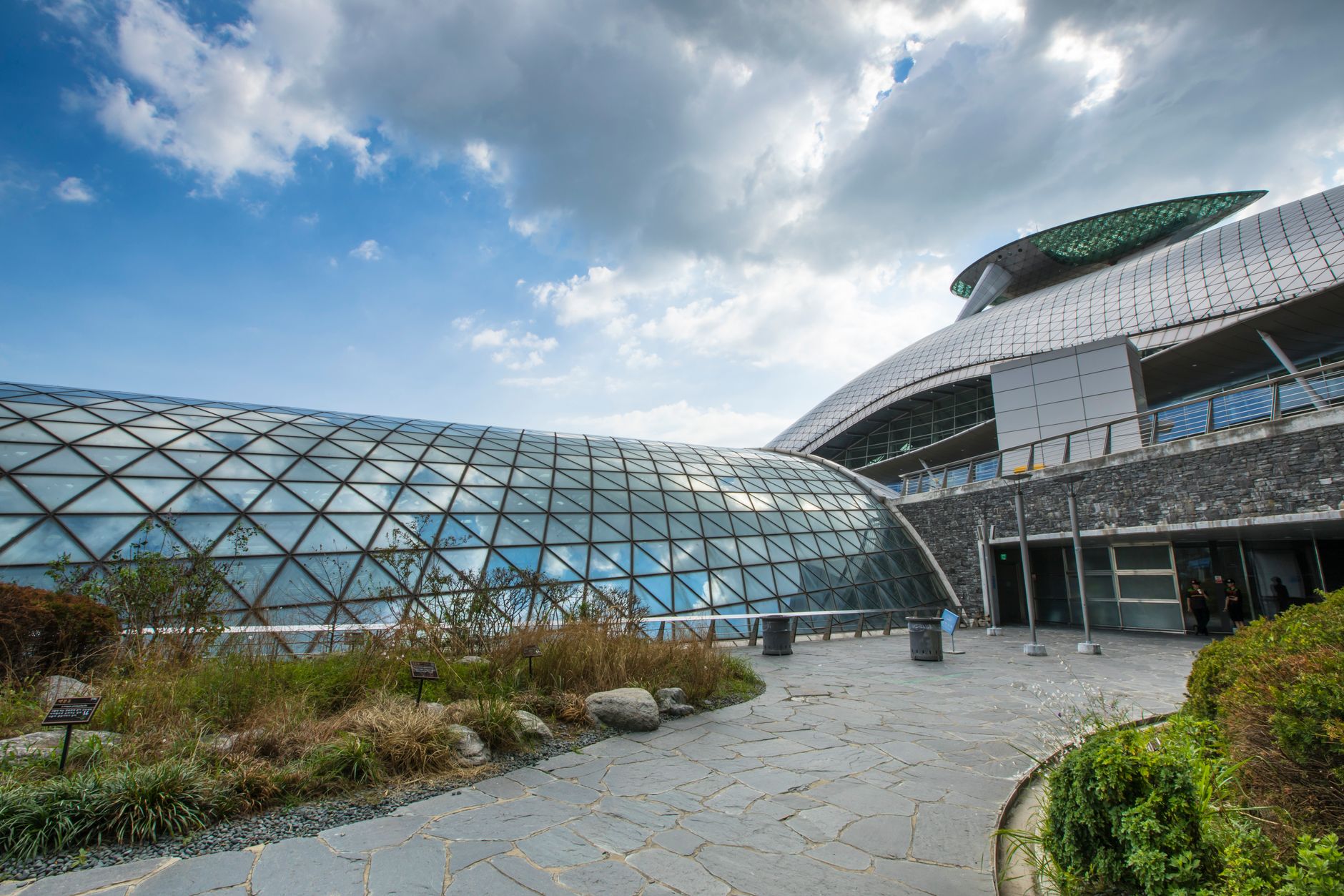 A stunning modern architectural structure featuring a glass dome and stone facade under a bright blue sky.