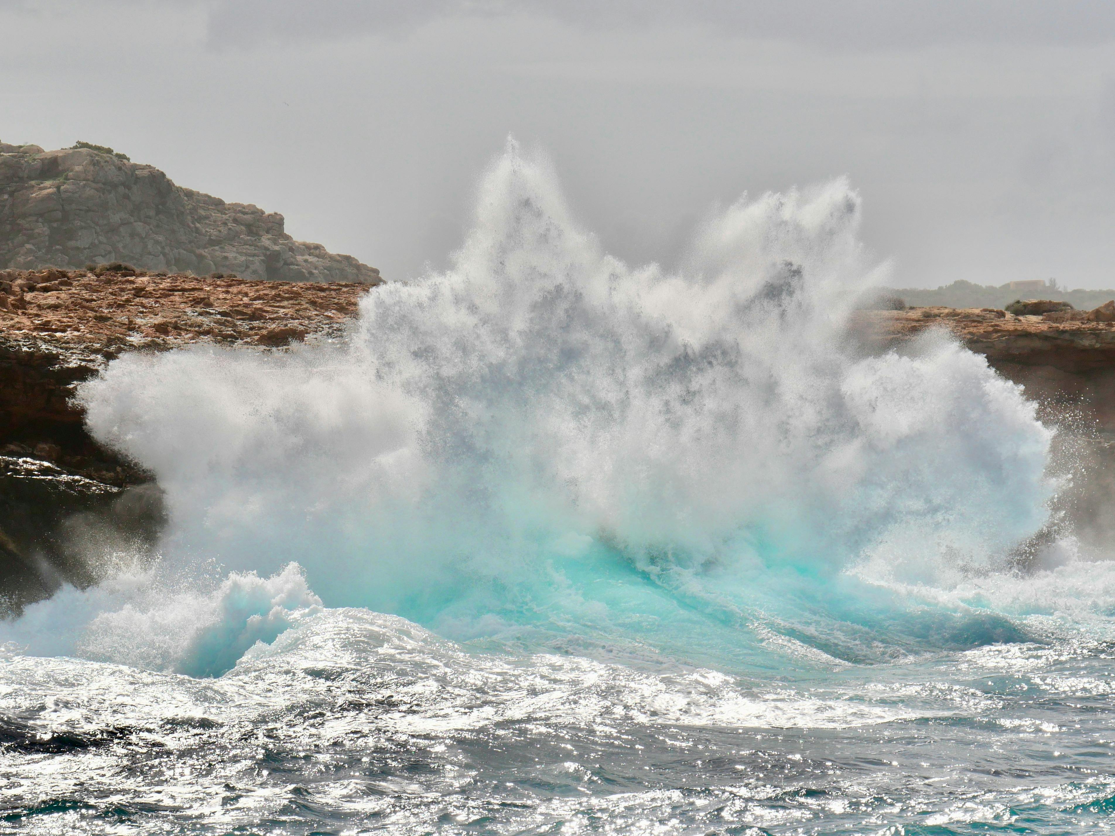 Powerful sea waves crash against rugged rocks, creating a stunning splash of turquoise water.