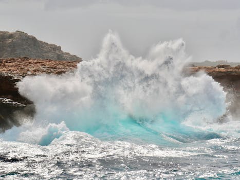 Powerful sea waves crash against rugged rocks, creating a stunning splash of turquoise water.