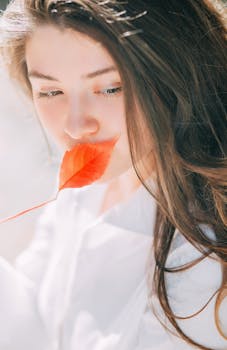 柔和的自然光中，一位长发女子手持红叶的肖像