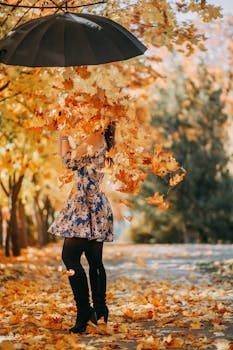 公园里，一名女子站在一把伞下，周围是鲜艳的秋叶，像是在开玩笑