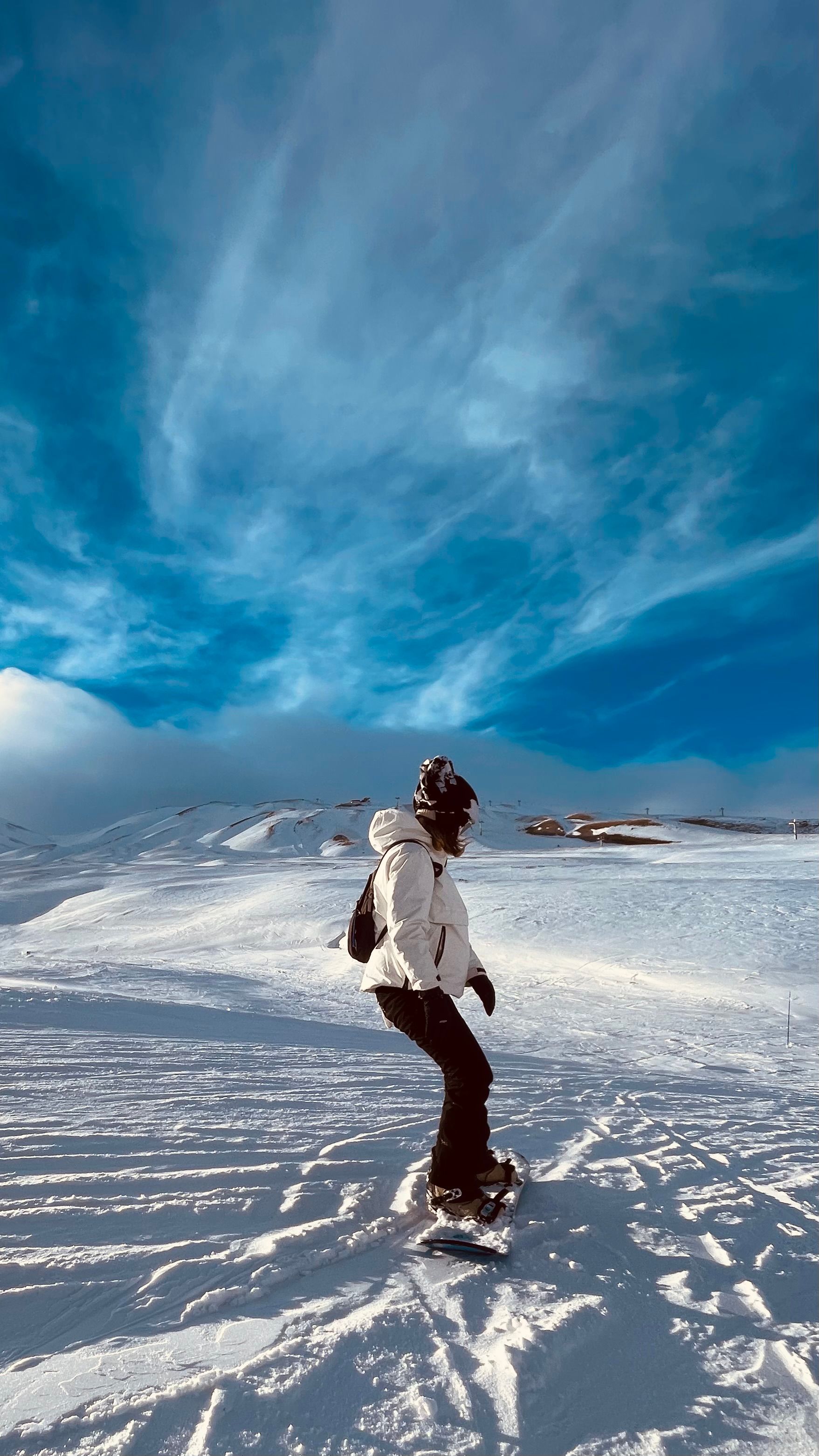 Snowboarder on snowy slopes under a clear blue sky at Erciyes Mountain, Türkiye.